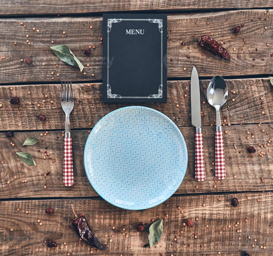 Dinner time. High angle shot of empty plate, fork, spoon, knife and closed menu lying on rustic table photo