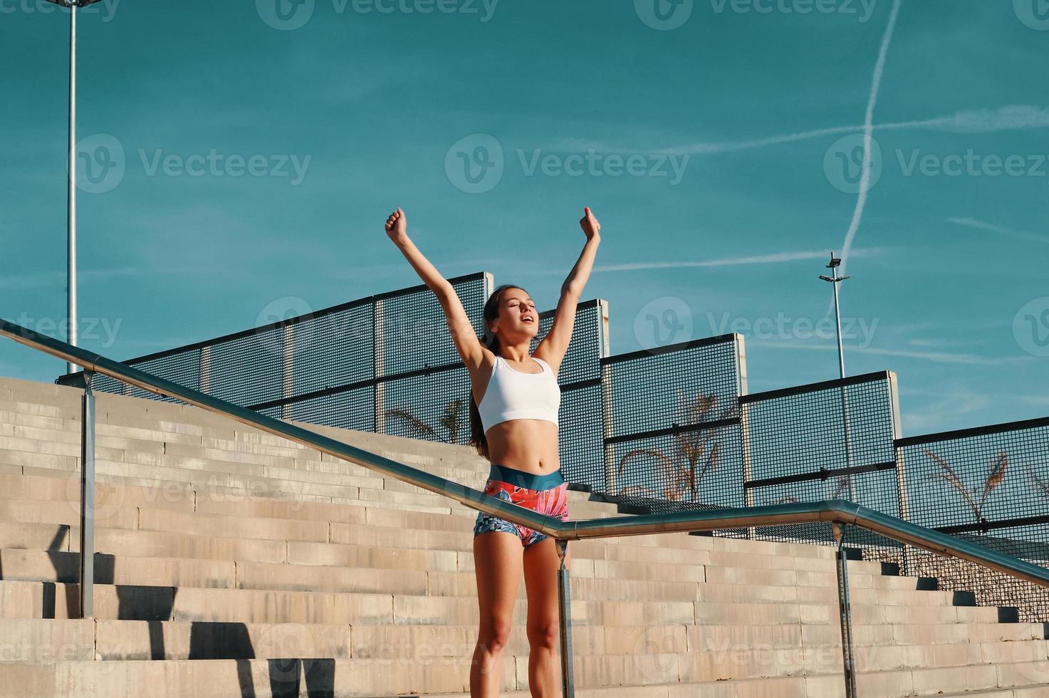 Beautiful young woman in sports clothing keeping arms outstretched while exercising outdoors photo