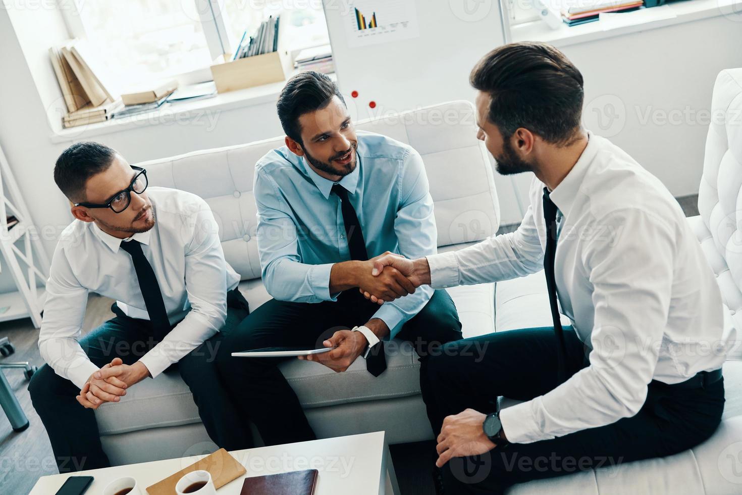 Welcome to our team Young modern men in formalwear shaking hands while working in the office photo