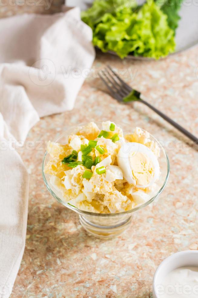 Potato salad with boiled egg, green onion and mayonnaise in a bowl on the table. Vertical view photo