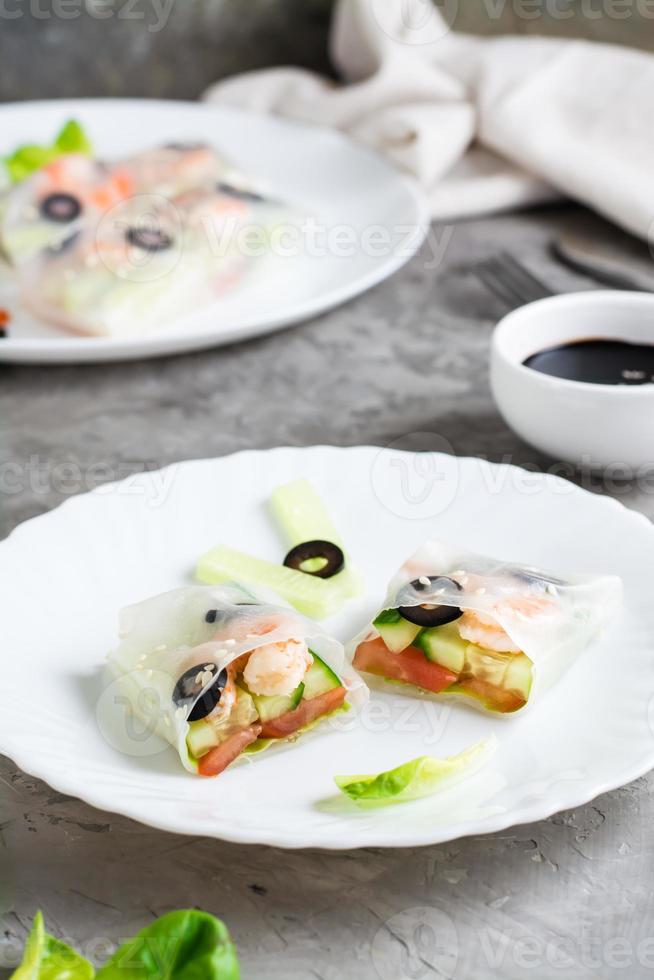 Spring roll cut in half in rice paper with seafood and vegetables on a plate. Vertical view photo
