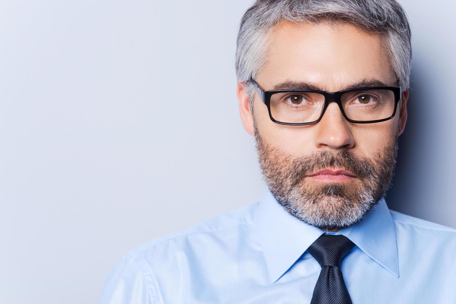 Portrait of confidence and success. Portrait of confident mature man in shirt and tie looking at camera and while standing against grey background photo