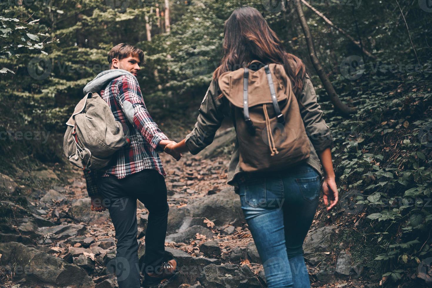 disfrutando del viaje. vista trasera de una pareja joven moderna tomándose de la mano y subiendo mientras caminan juntos por el bosque foto