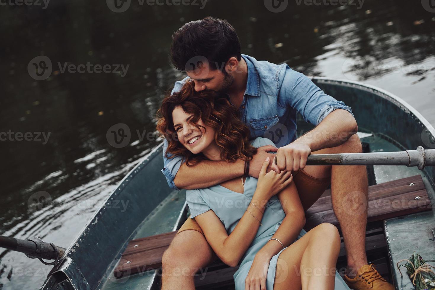 Made to love each other. Beautiful young couple embracing and smiling while enjoying romantic date on the lake photo