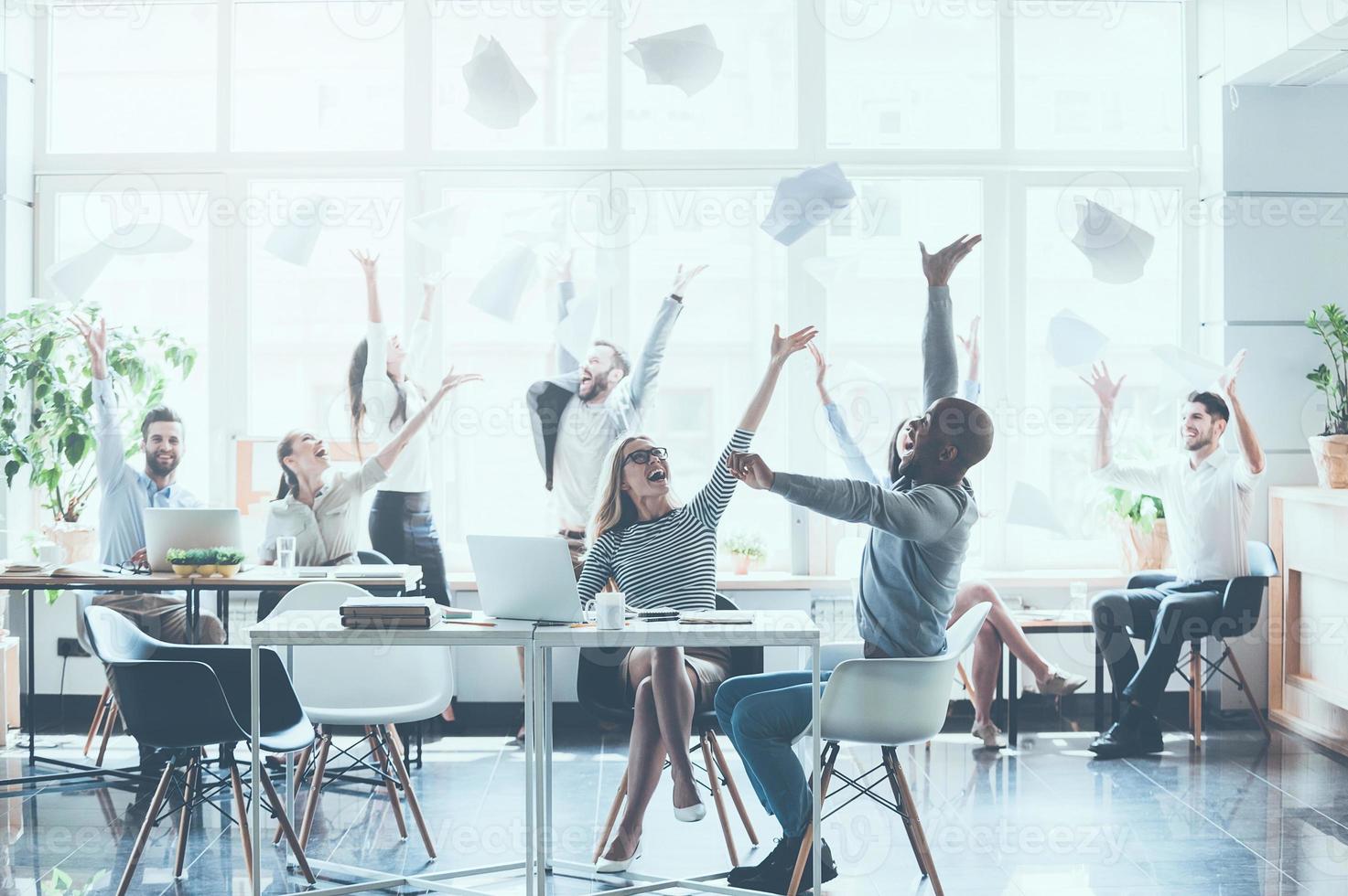 Celebrating success. Group of young business people throwing documents and looking happy while sitting at their working places in office photo