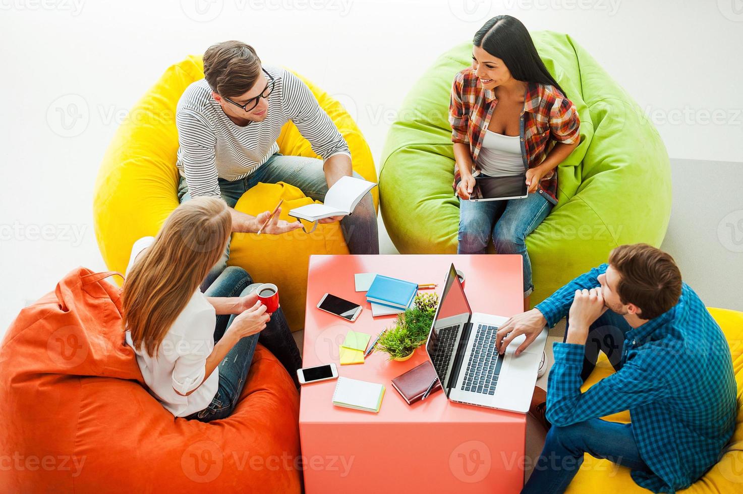 Place where ideas born. Top view of four young people working together while sitting at the colorful bean bags photo