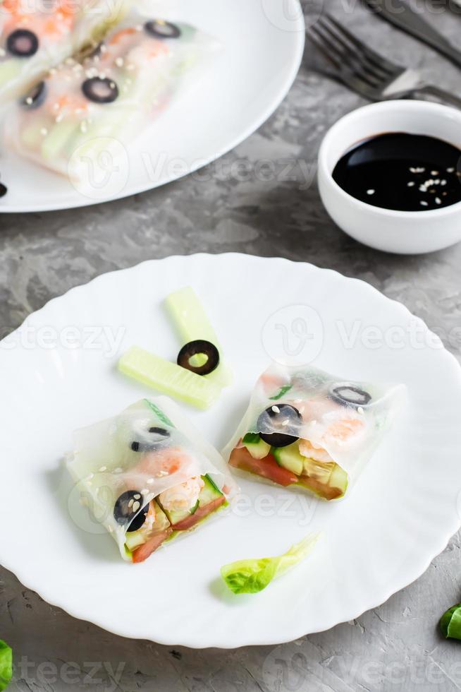 Spring roll cut in half in rice paper with seafood and vegetables on a plate. Close-up vertical photo