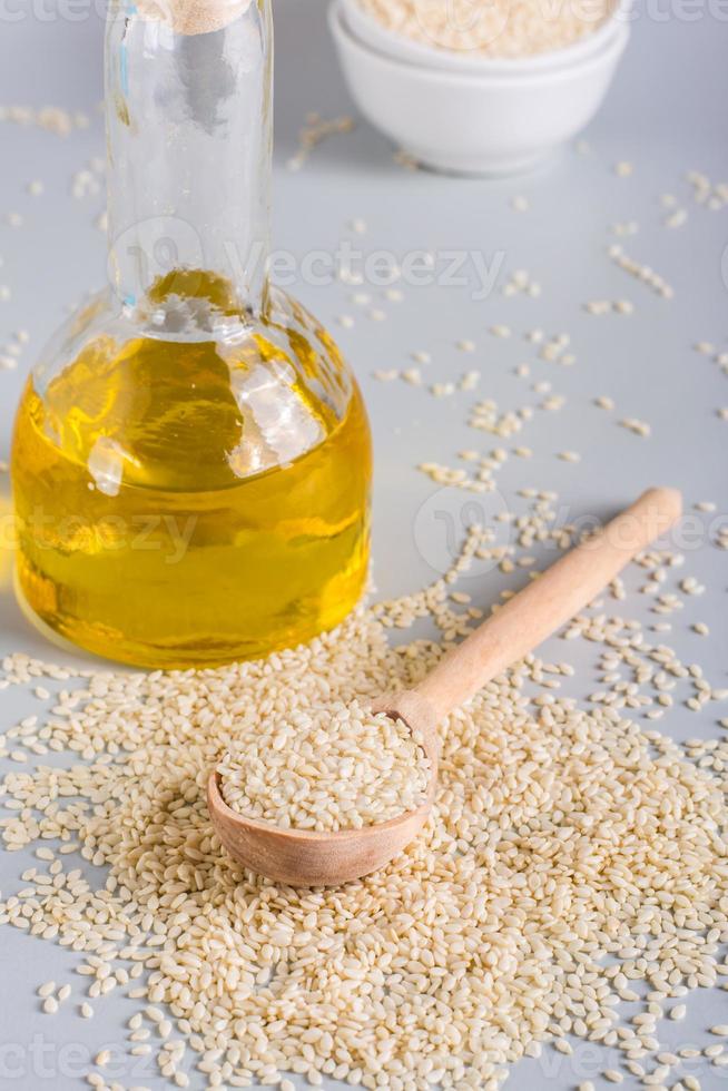 Sesame oil in a bottle and sesame seeds in a bowl on the table. Organic Alternative. Vertical. Closeup photo