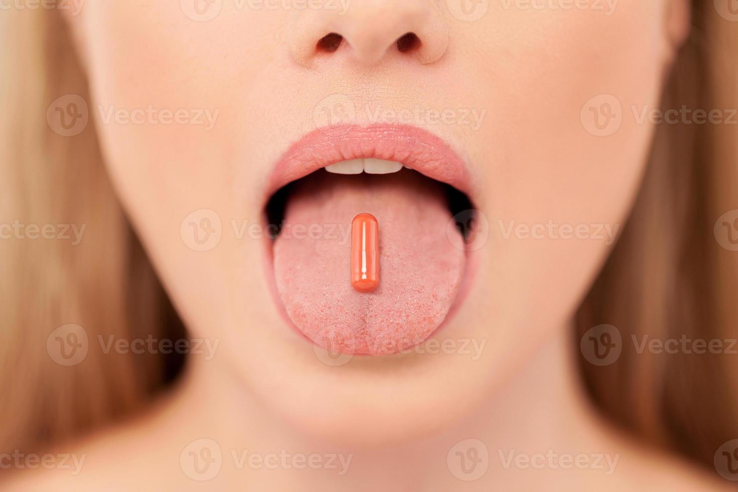 Pill on her tongue. Close-up of young woman holding pill on her tongue photo