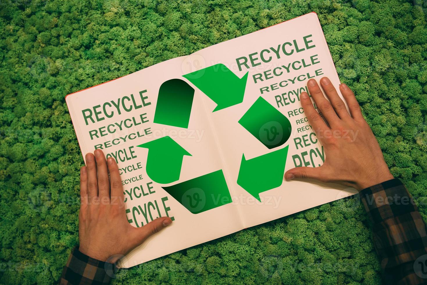 Step to green life. Top view close-up image of man holding hands on his notebook with recycle symbol and text at moss background photo