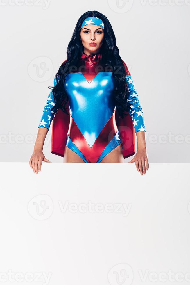 Statement from powerful woman. Beautiful young woman in superhero costume looking at camera and holding copy space while standing against white background photo