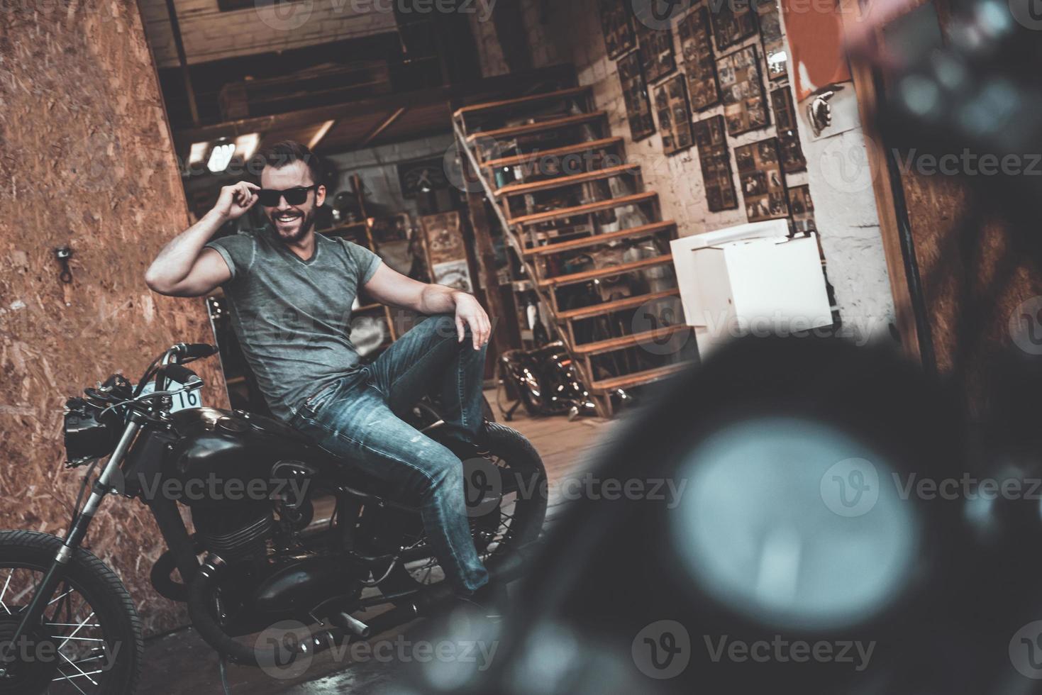 Confident biker. Handsome young man sitting on his bike with motorcycle garage in the background photo