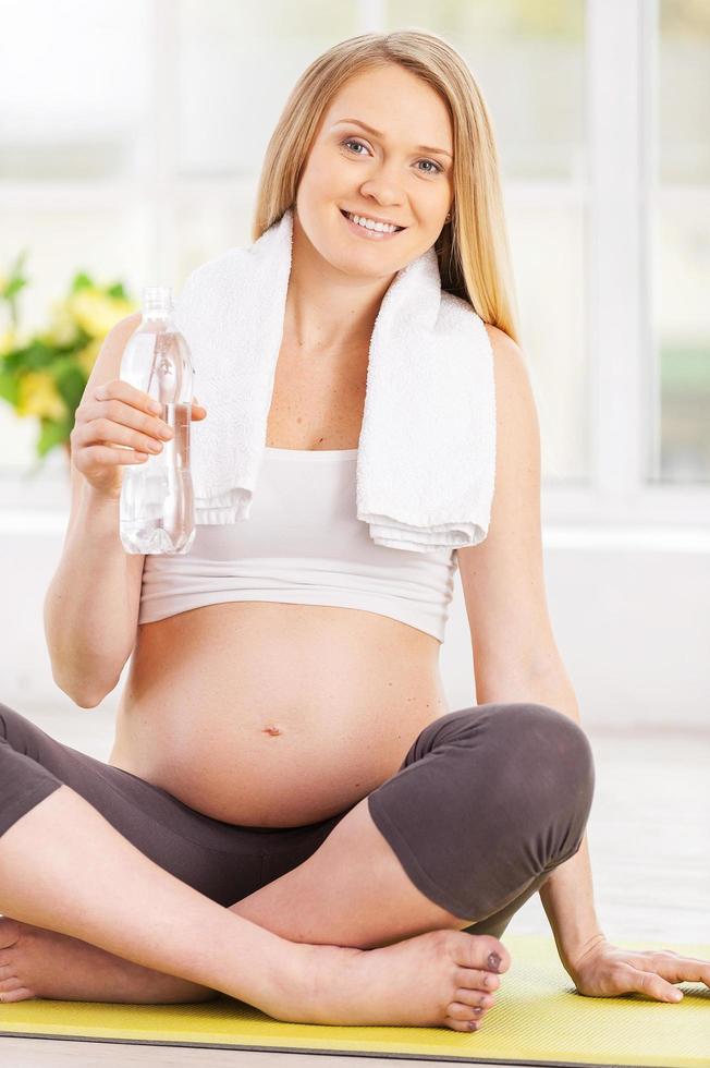 Clean water is important for my baby. Beautiful pregnant woman holding a bottle with water while sitting in lotus position photo