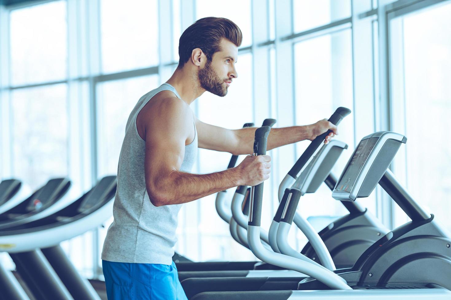 Working out for best body. Side view of young handsome man in sportswear looking away while working out on stepper at gym photo