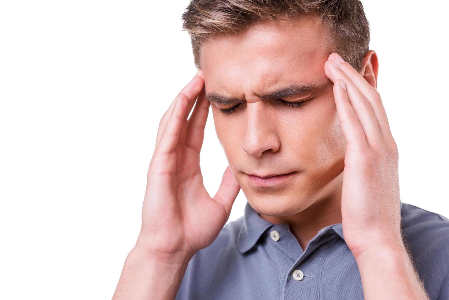 sintiendo un terrible dolor de cabeza. joven deprimido tocándose la cabeza con las manos y manteniendo los ojos cerrados mientras está aislado en el fondo blanco foto