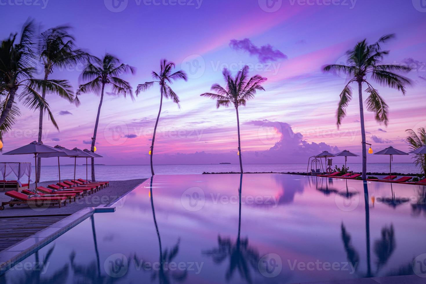 Luxury sunset over infinity pool in a summer beachfront hotel resort at beautiful tropical landscape. Tranquil beach holiday vacation background. Amazing island sunset beach view, palms swimming pool photo