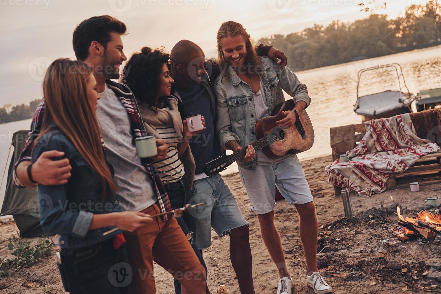 Best place to rest. Group of young people in casual wear smiling while enjoying beach party near the lake photo