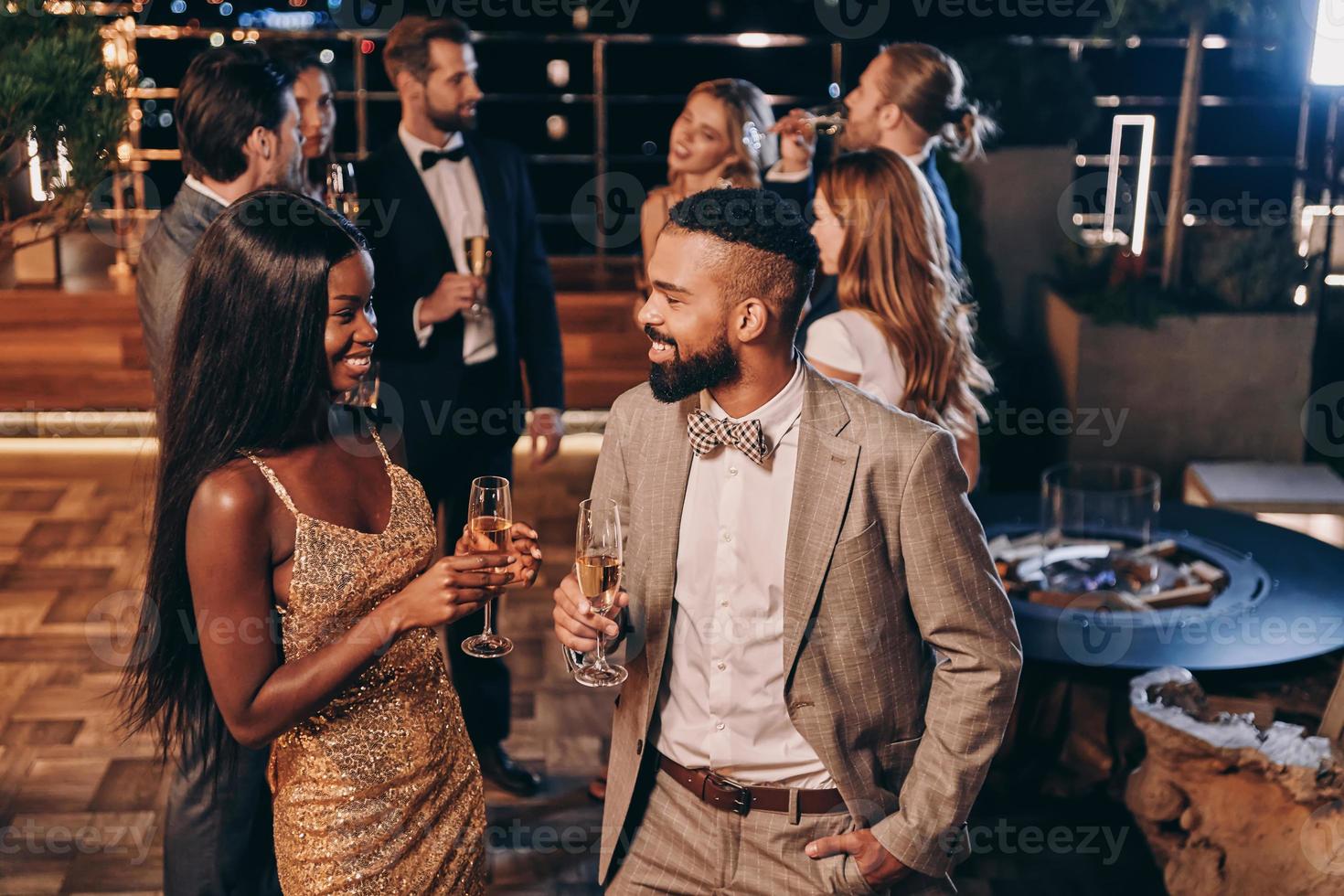 hermosa joven pareja africana en ropa formal sosteniendo flautas de champán y sonriendo foto