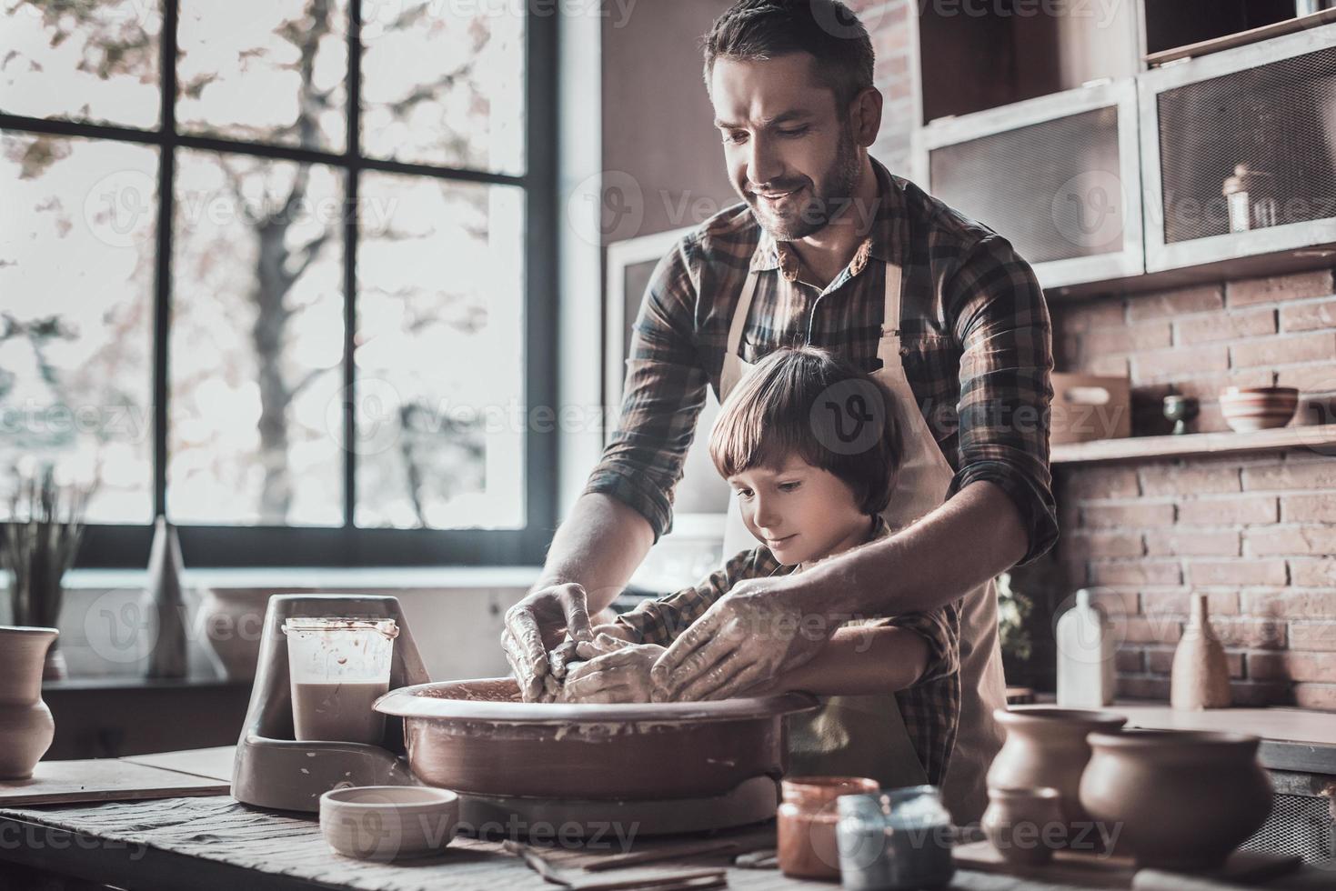 aprendiendo nuevas habilidades del padre. joven alegre y niño pequeño haciendo vasijas de cerámica en la clase de cerámica foto