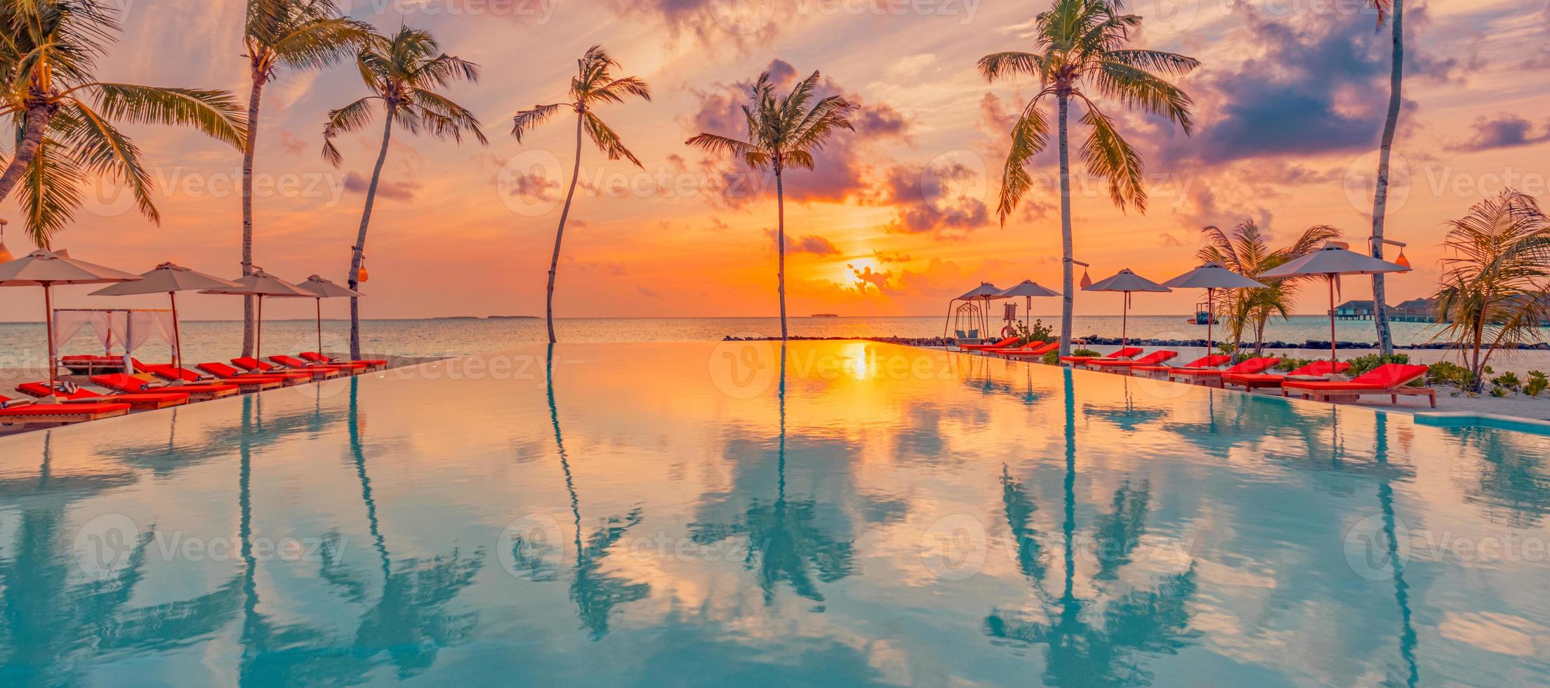 Luxury sunset over infinity pool in a summer beachfront hotel resort at beautiful tropical landscape. Tranquil beach holiday vacation background. Amazing island sunset beach view, palms swimming pool photo