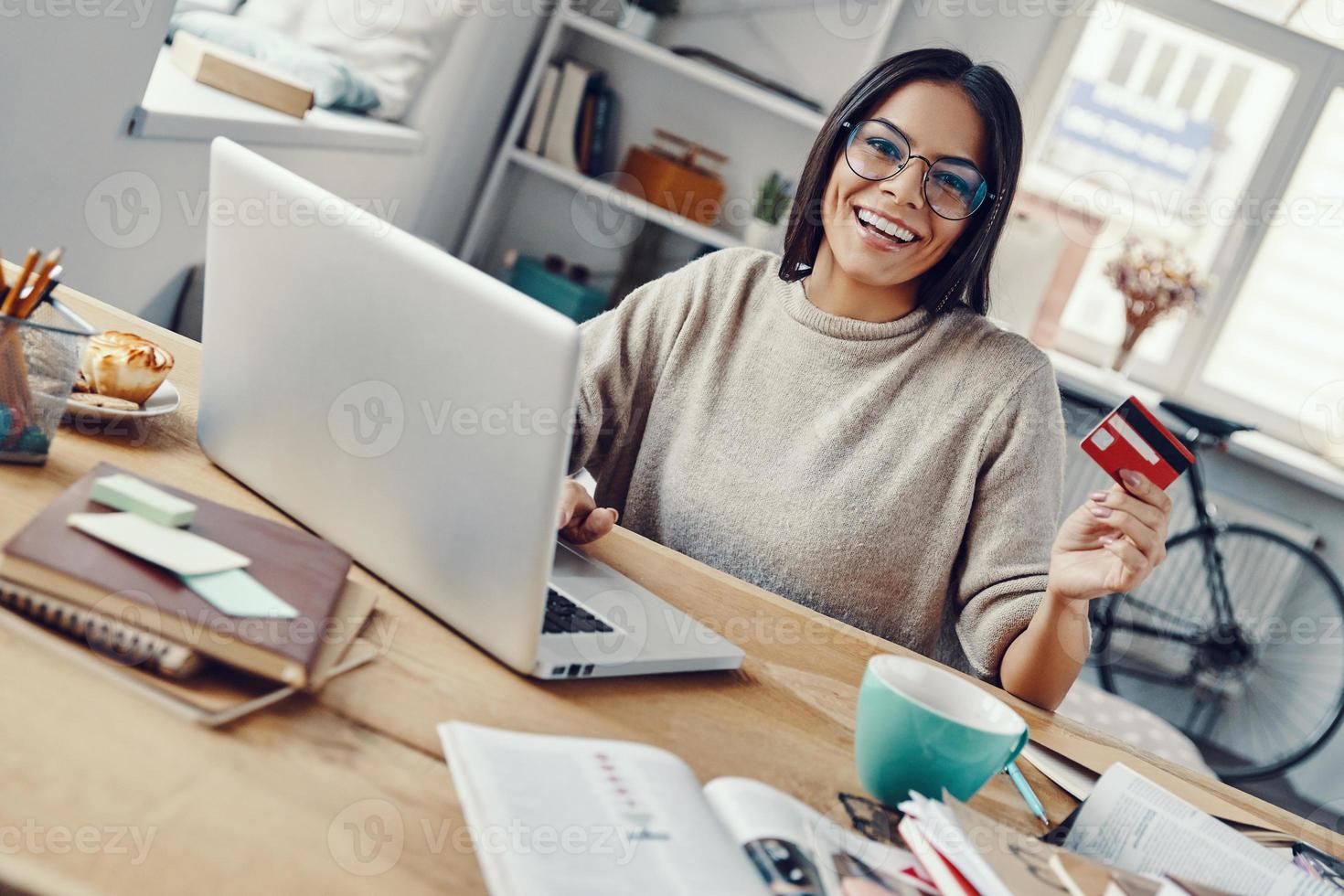 bella joven con ropa informal comprando en línea usando una laptop mientras está sentada en el interior foto