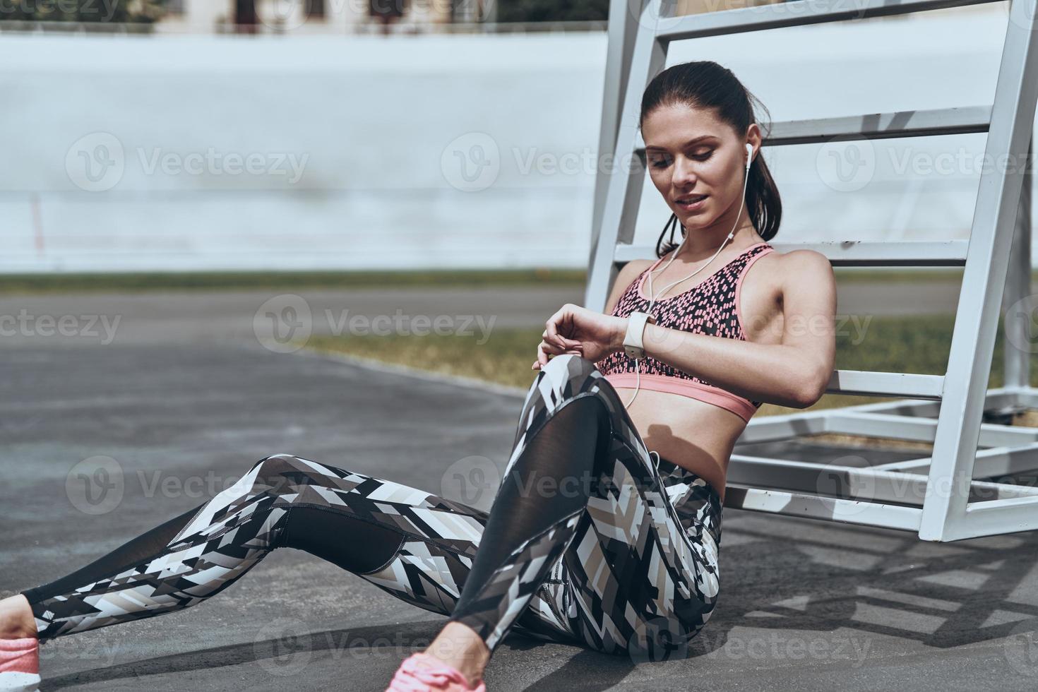 Checking the results. Beautiful young woman in sports clothing checking the pedometer while sitting outdoors photo