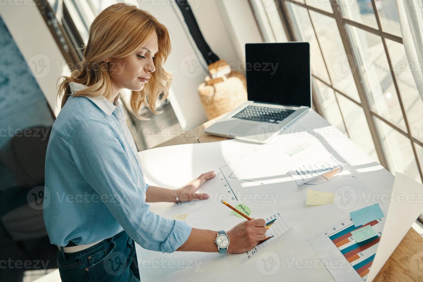 Top view of confident young woman sketching on the blueprint while working in office photo