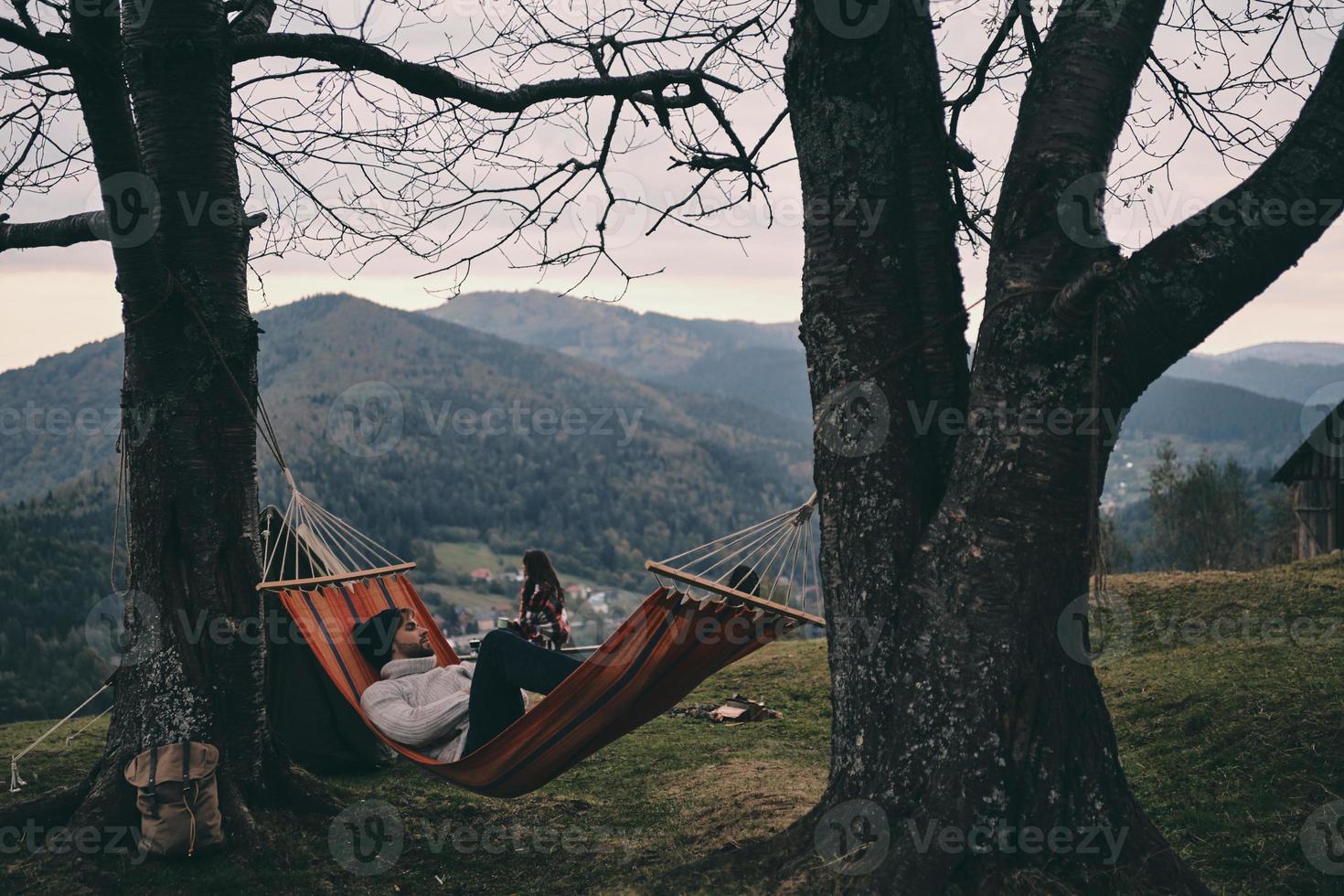 descansando después de un largo camino. apuesto joven acostado en una hamaca mientras acampa con su novia foto