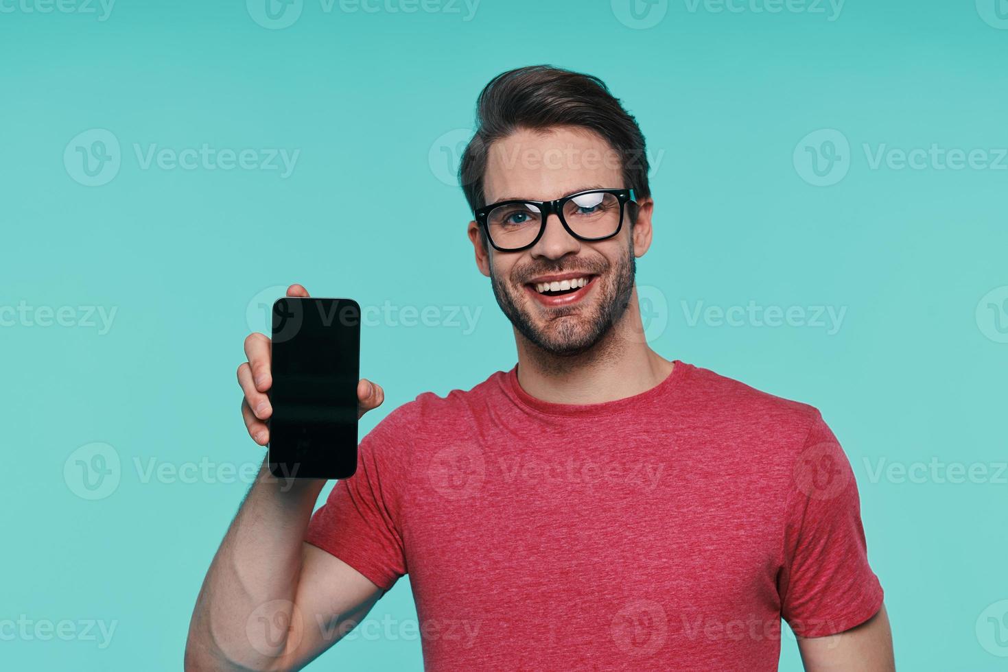 Portrait of handsome young man in eyeglasses showing his smart phone and smiling photo