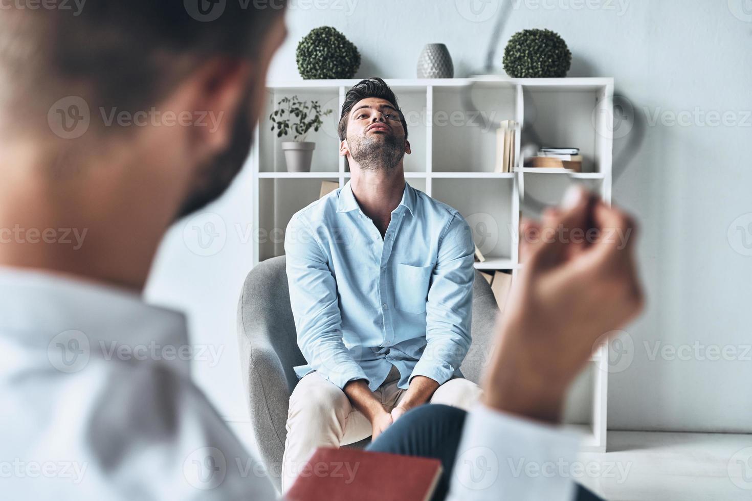 Totally lost. Young frustrated man solving his mental problems while having therapy session with psychologist photo