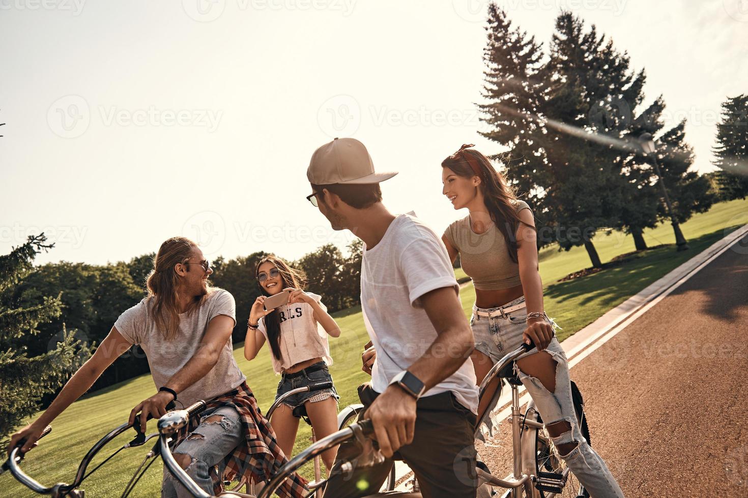 They will remember this day. Group of happy young people in casual wear photographing while cycling together outdoors photo