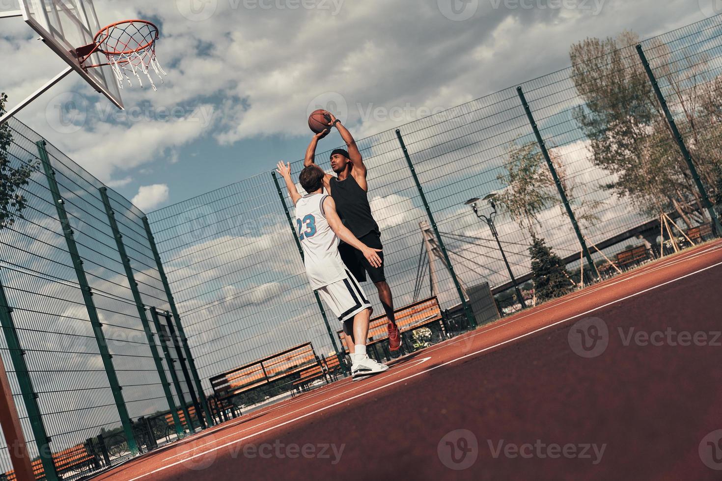 Playing basketball. Two young men in sports clothing playing basketball while spending time outdoors photo