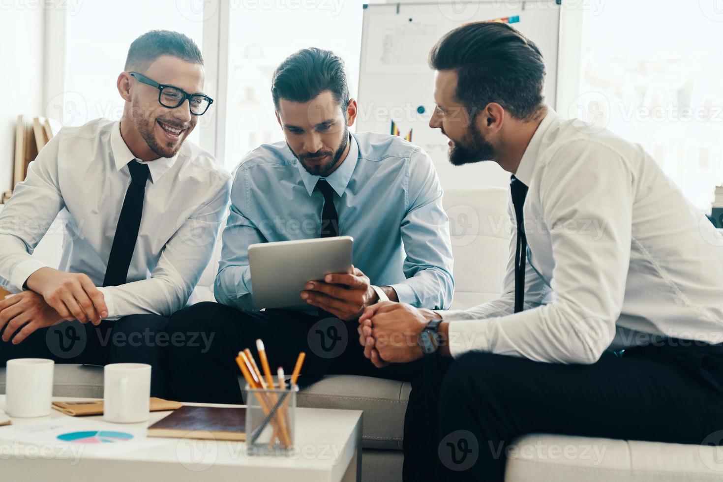 Brainstorming together. Group of young modern men in formalwear working using digital tablet while sitting in the office photo