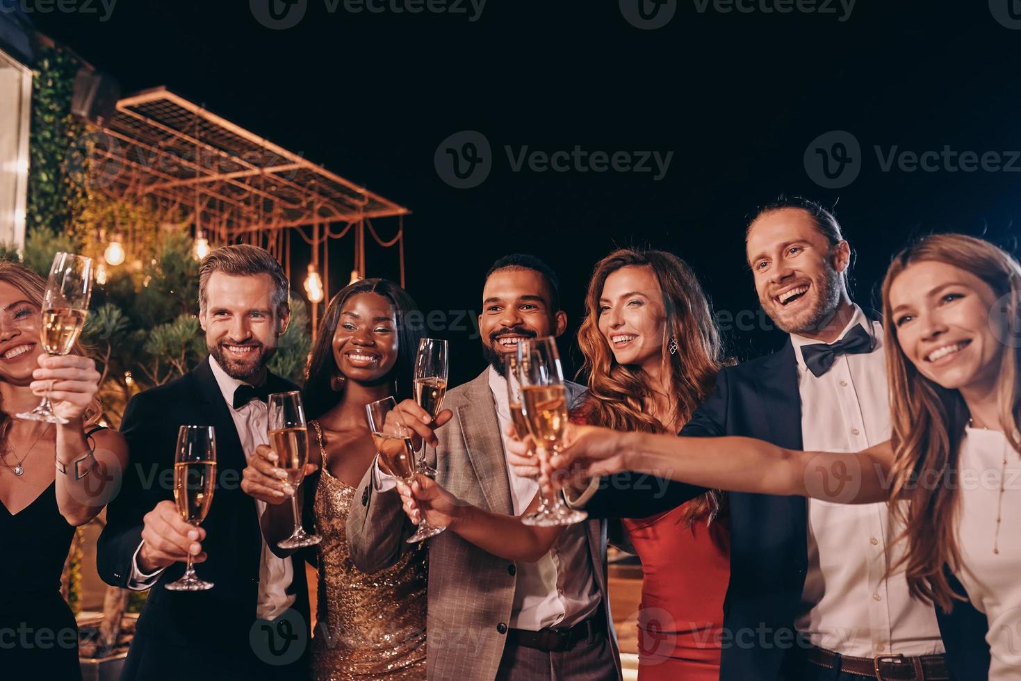 Group of people in formalwear toasting with champagne and smiling while spending time on luxury party photo