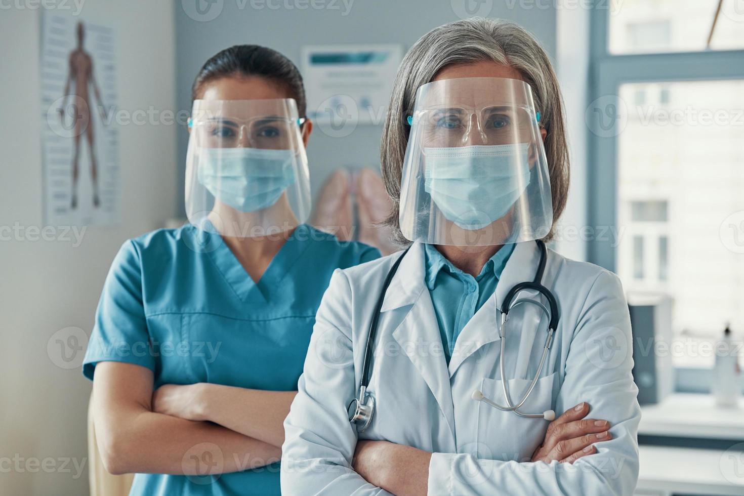 dos compañeras de trabajo con uniforme médico y ropa de trabajo protectora con los brazos cruzados y mirando la cámara mientras trabajan en el hospital foto