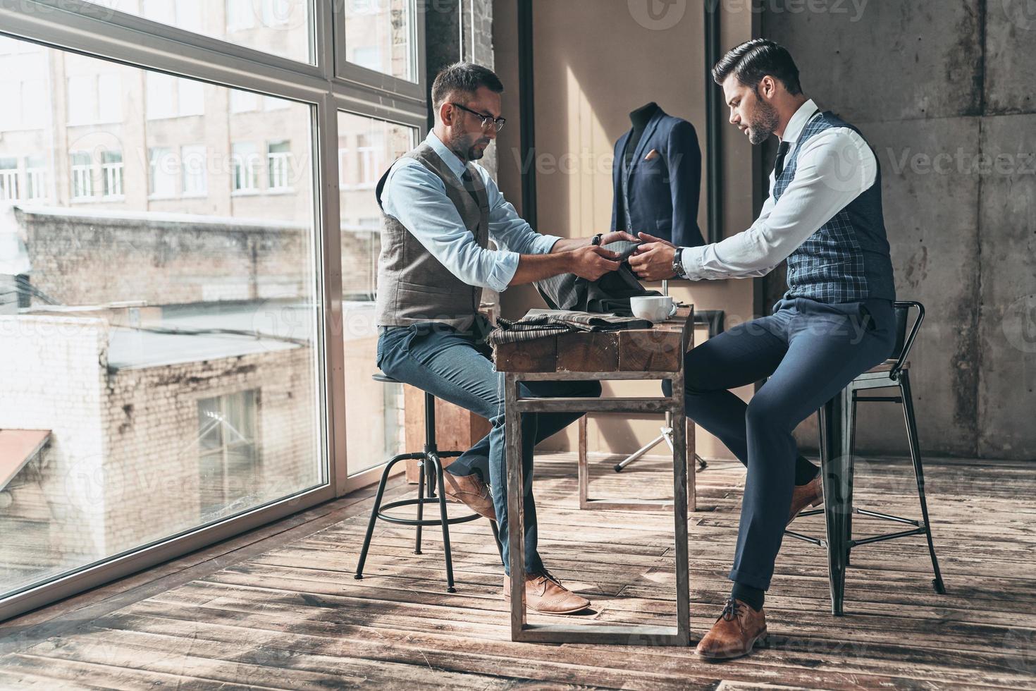 Hard choice. Young fashionable designer choosing fabric with his client while sitting in the workshop photo