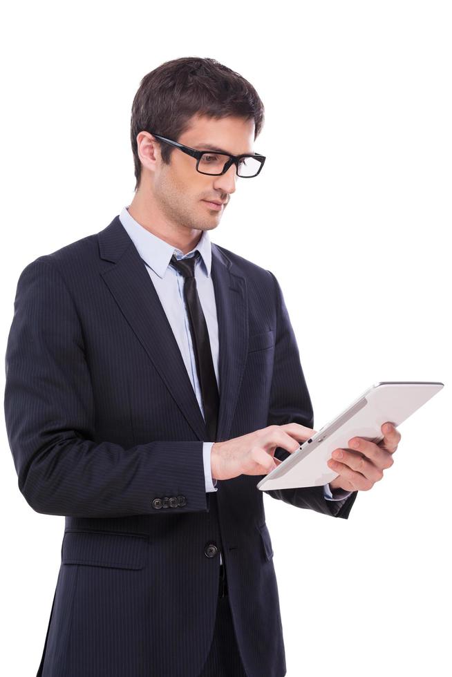 Businessman with digital tablet. Handsome young man in formalwear working on digital tablet while standing isolated on white background photo