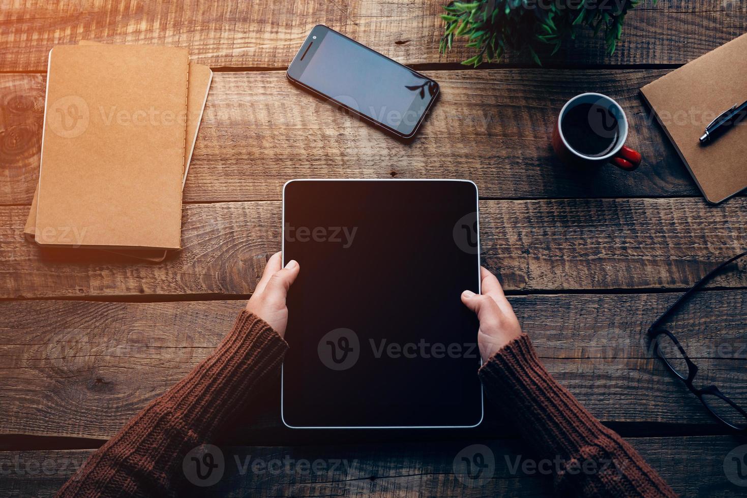 Technologies make life easier. Close-up top view image of woman holding digital tablet with copy space while sitting at the rough wooden table photo