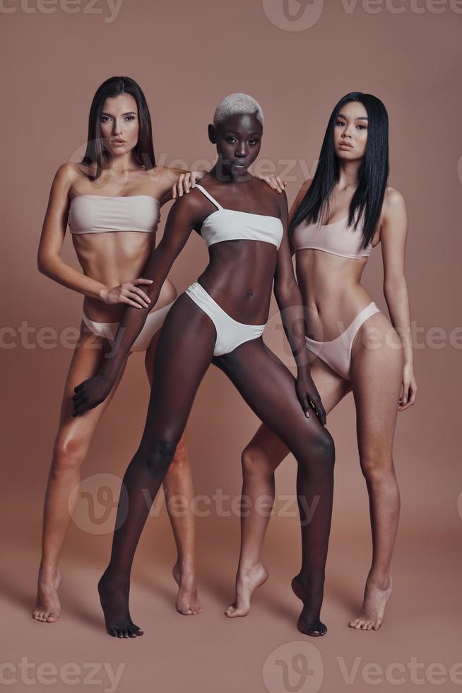 Looking amazing Full length of three attractive mixed race women looking at camera while standing against brown background photo