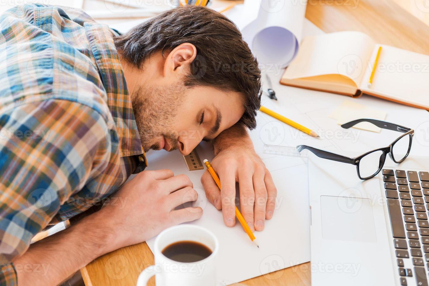 Feeling exhausted. Top view of young man sleeping while sitting at his working place photo