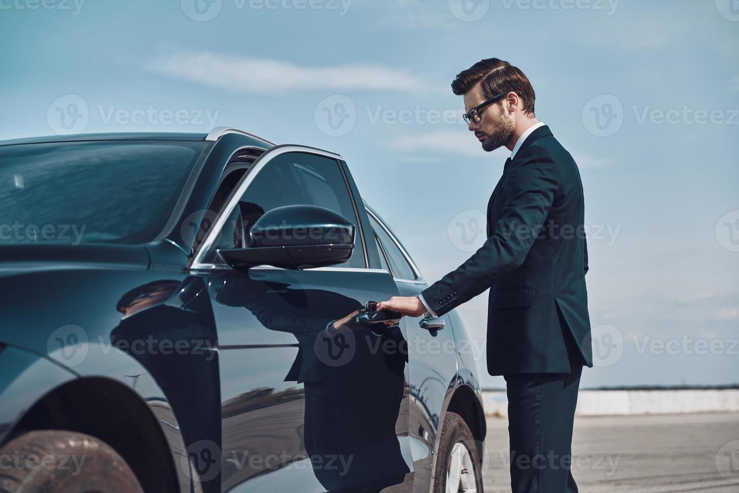 Status car owner. Handsome young businessman entering his car while standing outdoors photo