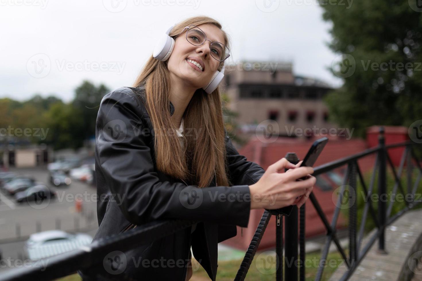 una joven hermosa con auriculares escucha música con un teléfono en las manos mira soñadoramente hacia arriba foto