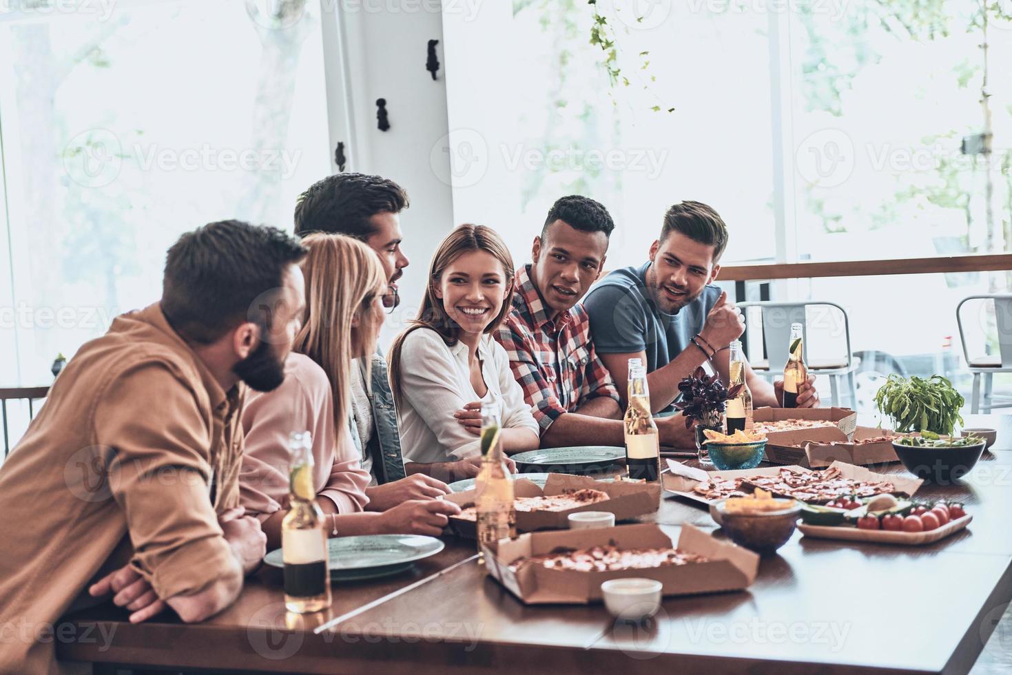 Close friends. Group of young people in casual wear communicating and smiling while having a dinner party photo