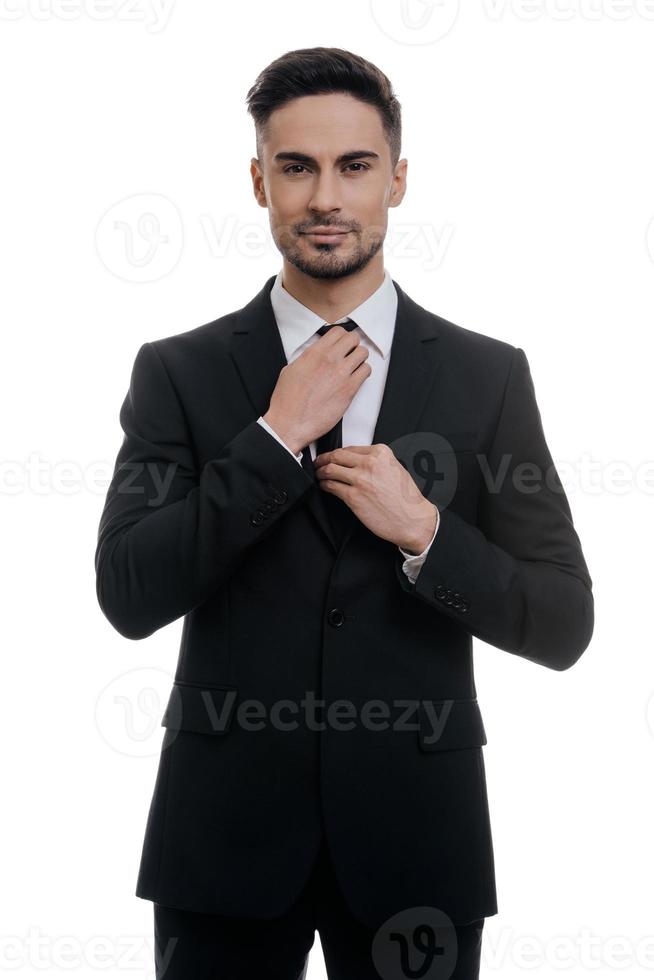 Used to look perfect. Handsome young man in full suit adjusting his necktie and looking at camera while standing against white background photo