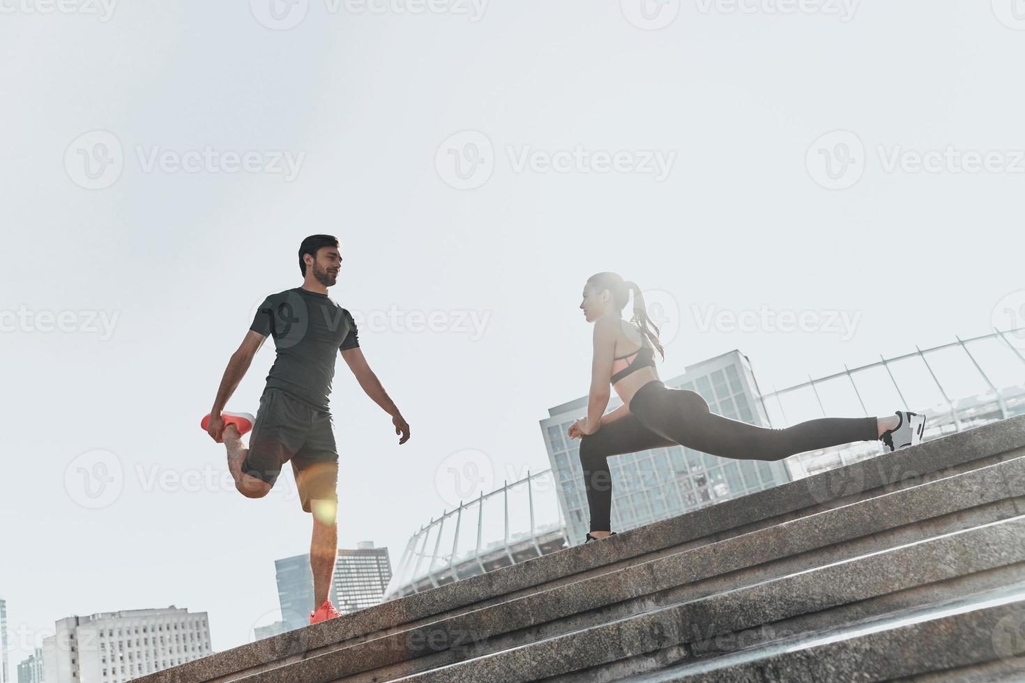 preparación de los músculos para las acciones. toda la longitud de una pareja joven con ropa deportiva haciendo ejercicios de estiramiento juntos foto