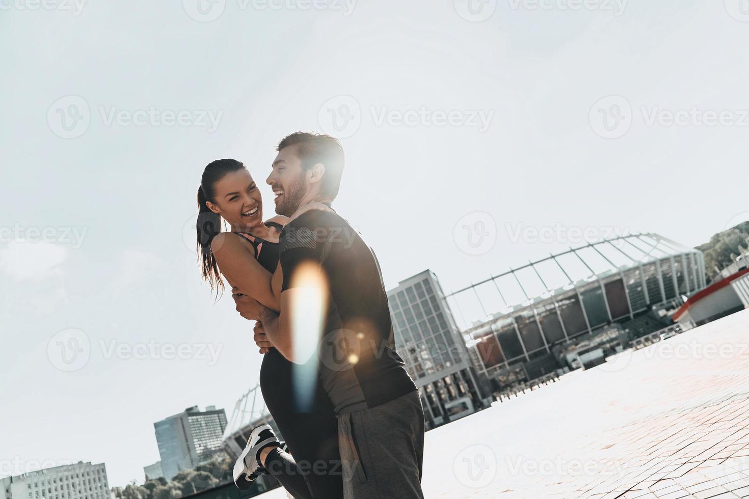 alegría de estar enamorado. hermosa pareja joven en ropa deportiva uniéndose y sonriendo mientras está de pie afuera foto