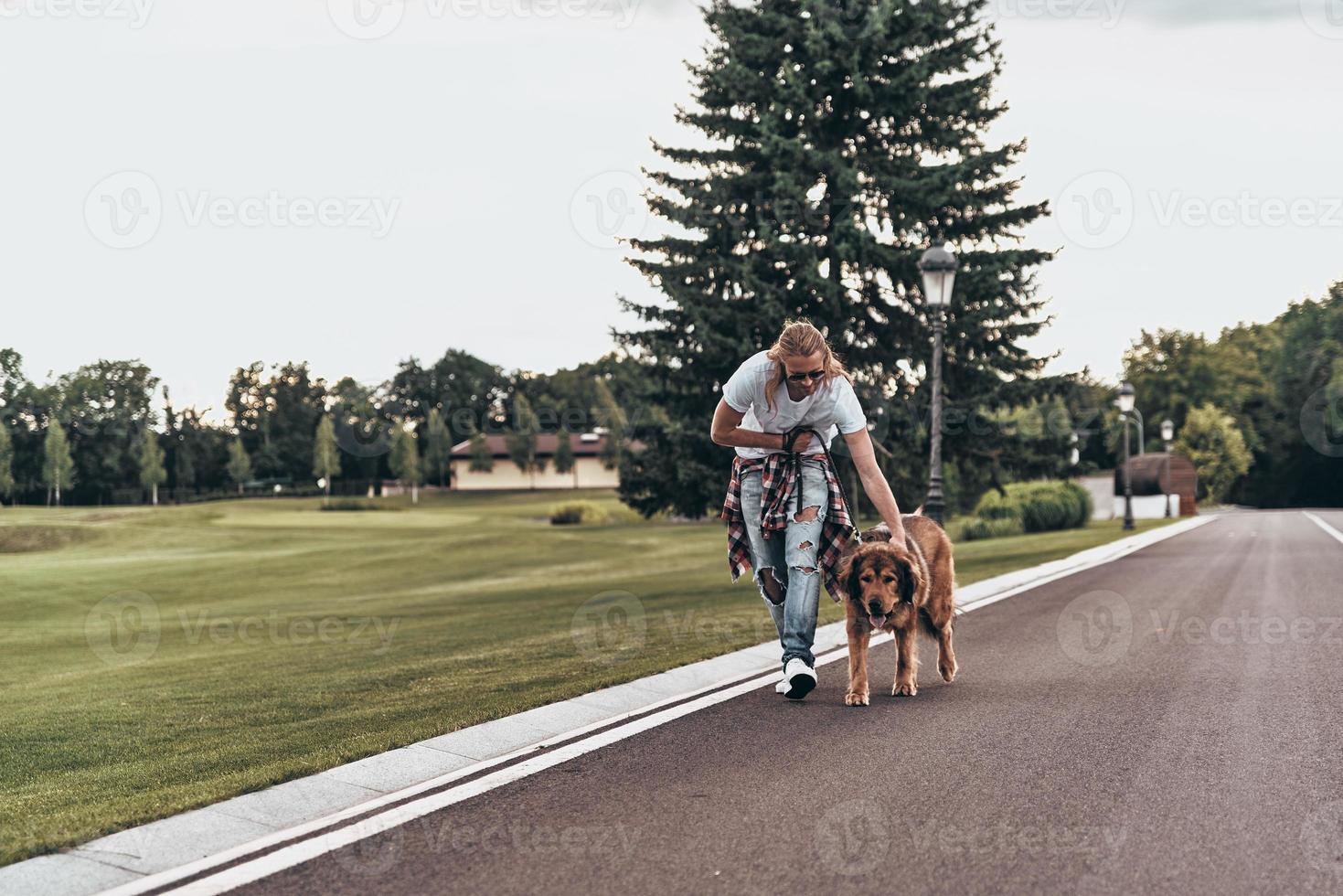 Time for a walk. Full length of handsome young man walking with his dog while spending time outdoors photo