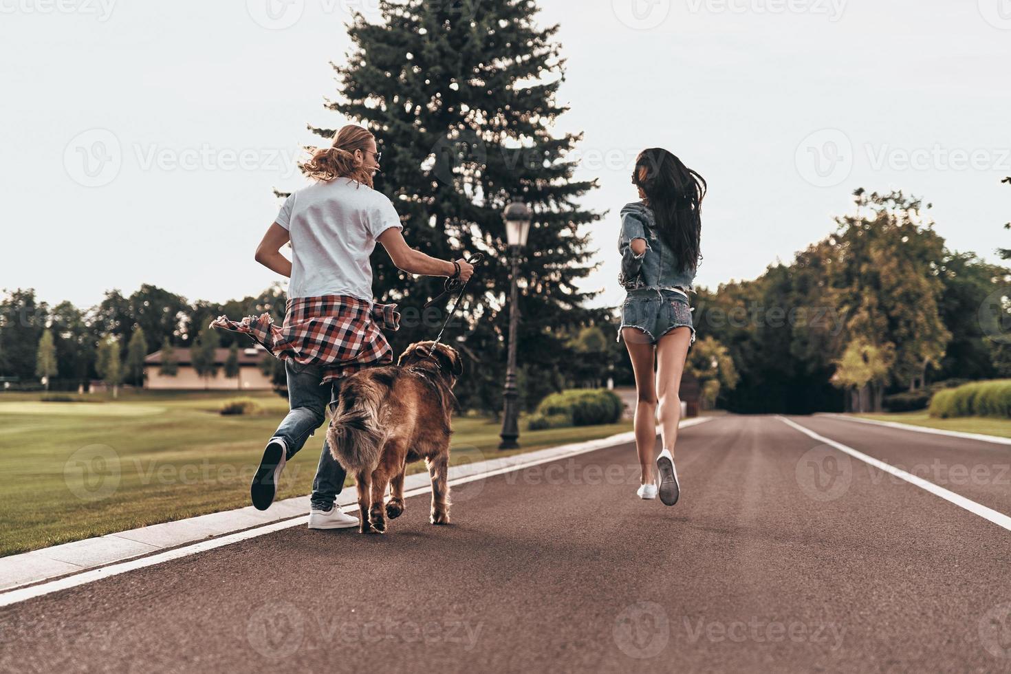 Going crazy together. Full length rear view of beautiful young couple running with their dog while spending time outdoors photo