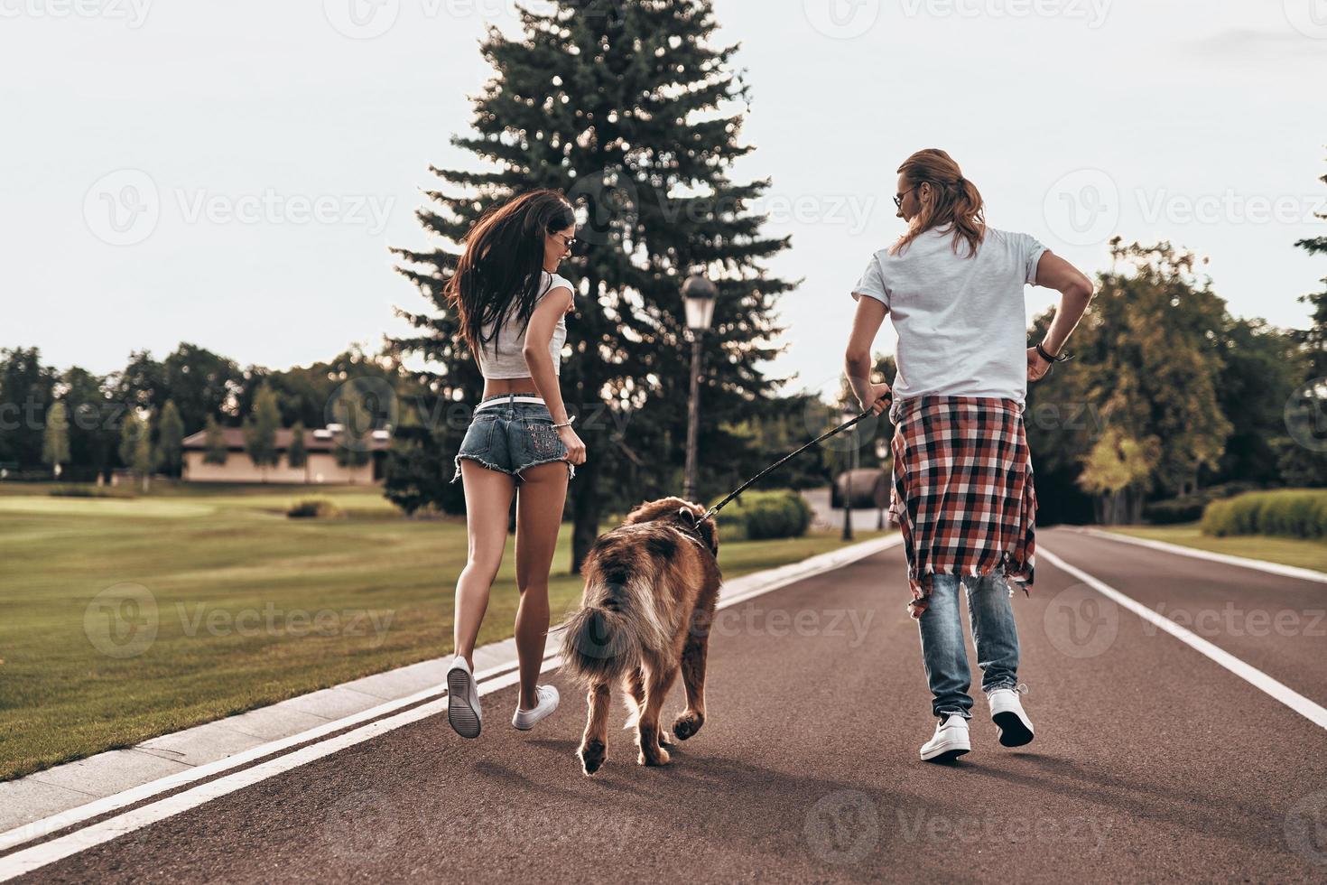 Playful and filled with love. Full length rear view of beautiful young couple running with their dog while spending time outdoors photo