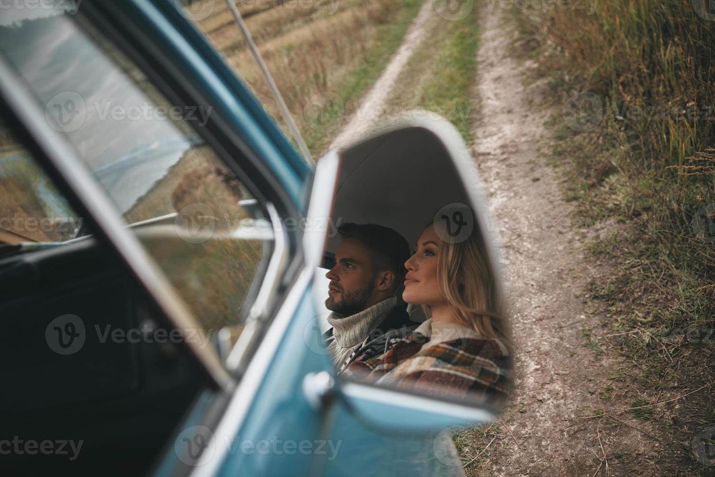 Happy couple traveling. Reflection of beautiful young couple looking away and smiling while sitting in retro style mini van photo